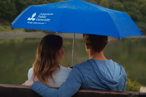 A couple sitting on a bench under an APU umbrella