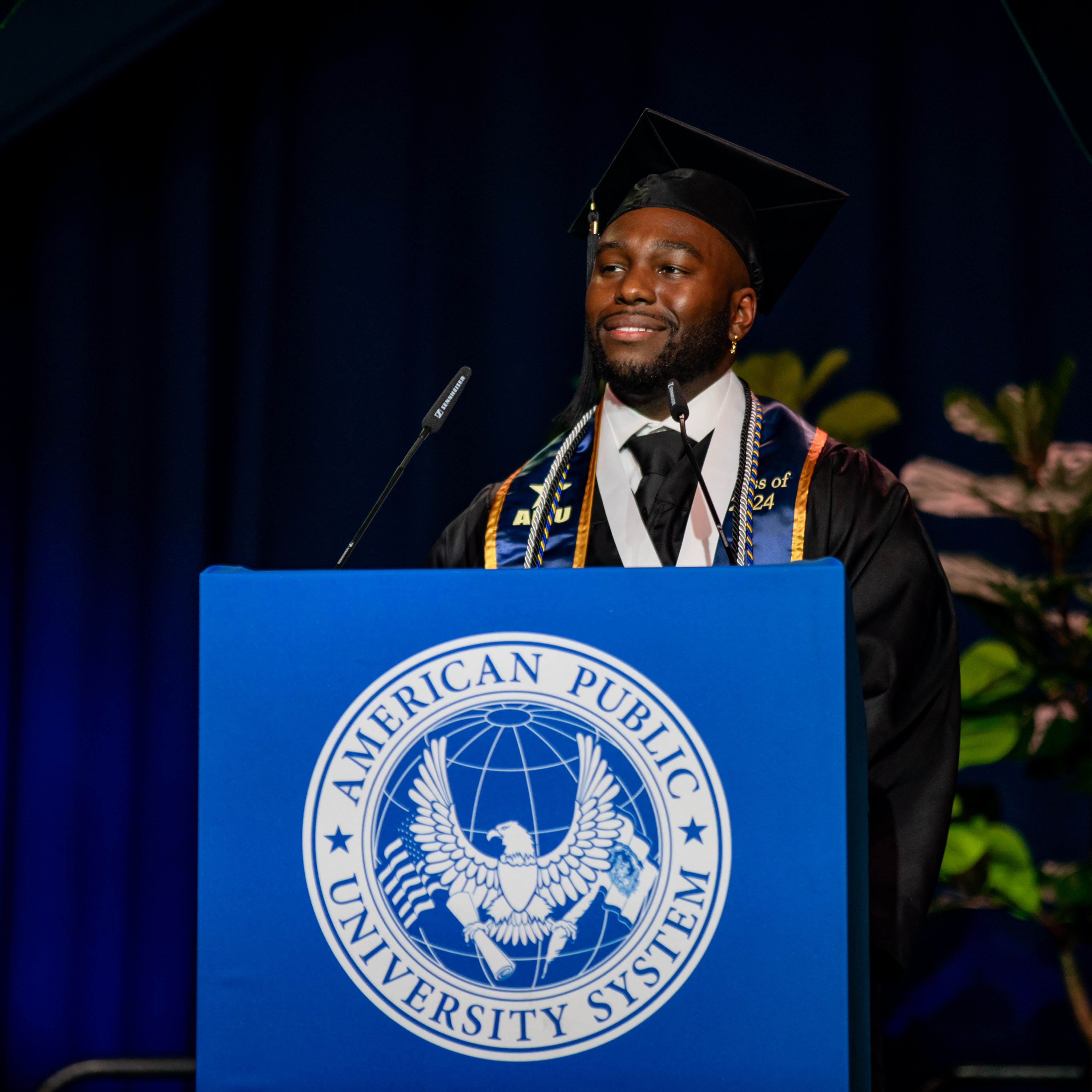 Man in graduation cap and gown giving speech during ceremony